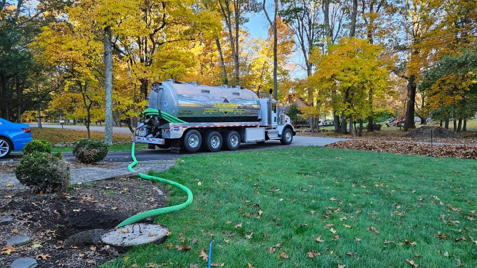 A Black Diamond tanker truck on a residential lawn with the suction hose run out to the septic tank