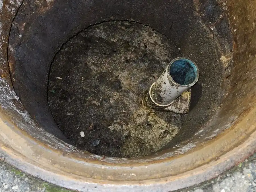 Looking down into an open concrete septic tank during a pump-out, inlet pipe visible against the tank wall