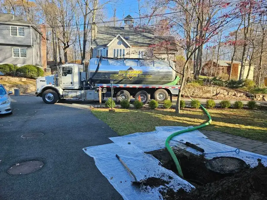 A protective tarp laid over the lawn beside an open septic lid with the suction hose in place